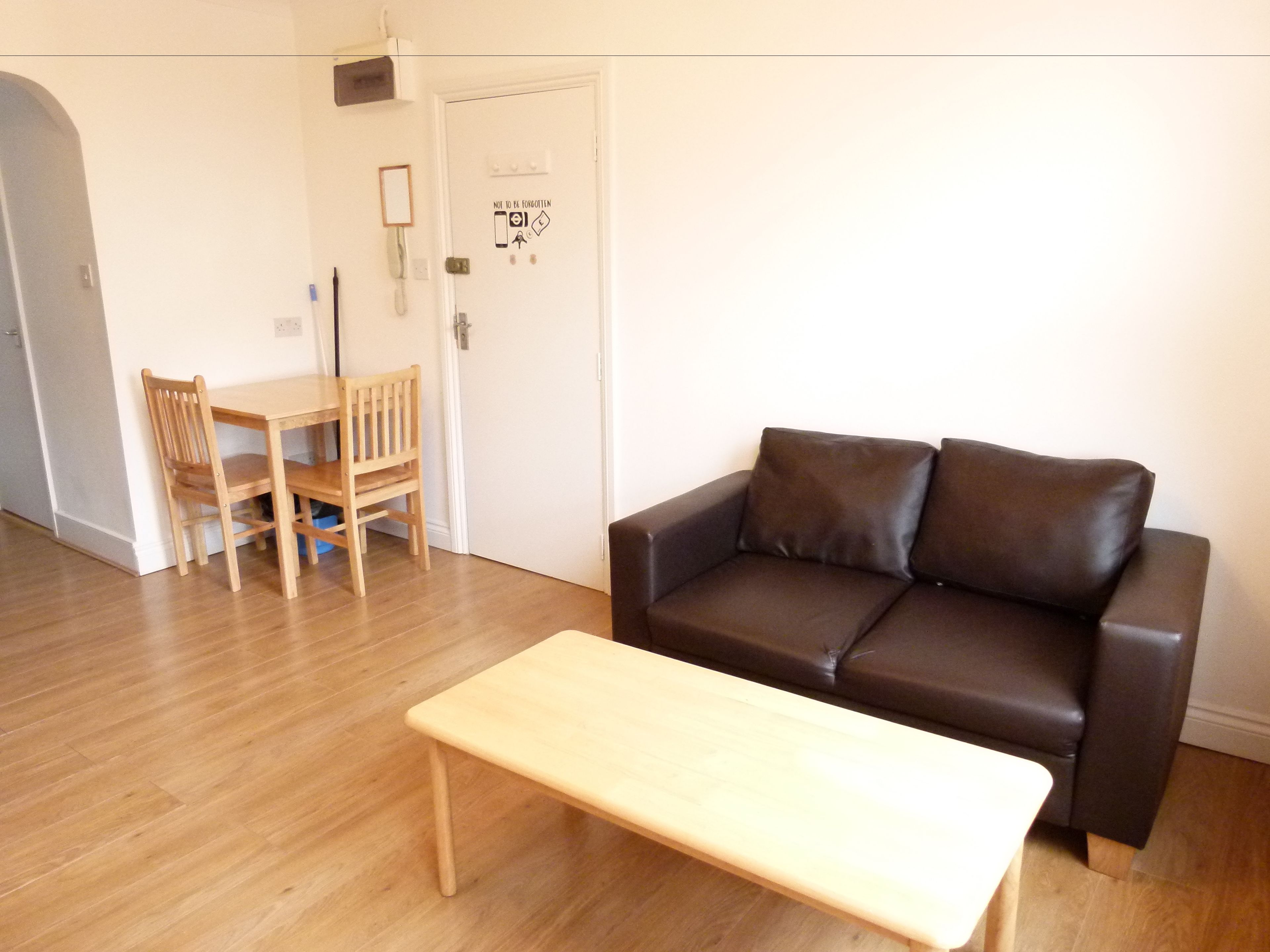 A living room with a brown leather sofa, a wooden coffee table, and a wooden dining table with chairs.