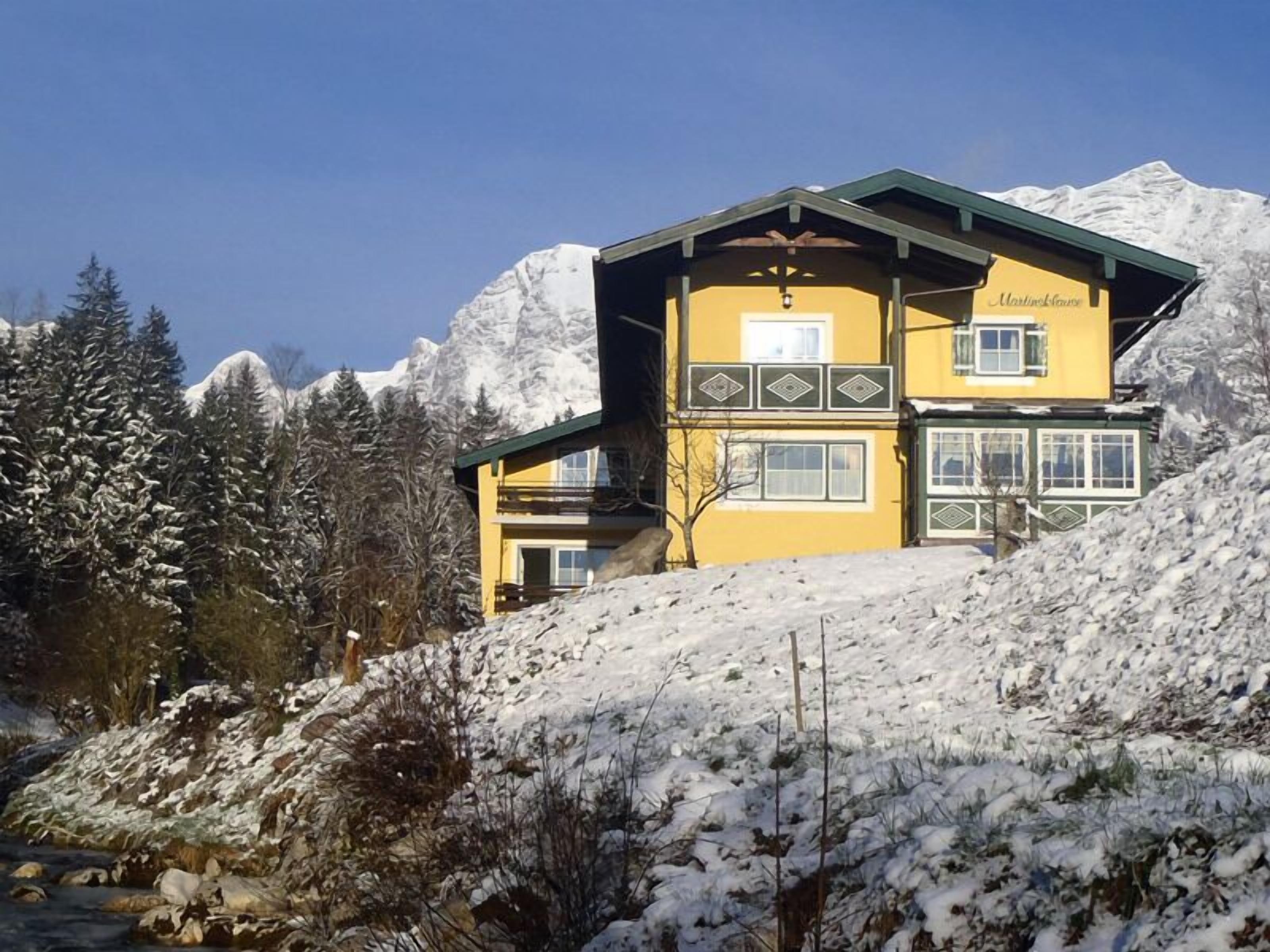 A two-story mountain lodge with a yellow facade, multiple windows, and a sign reading "Martinshaus".