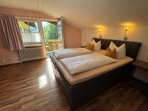 Un dormitorio con una cama grande, una ventana con cortinas, un radiador y suelo de madera.