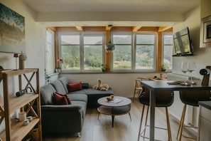 A cozy living area with a sofa, a round coffee table, and a dining table with chairs. Large windows offer a view of the outdoors.