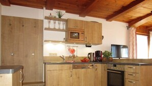 Una cocina con armarios de madera, microondas, cafetera y televisor.