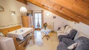 A cozy, well-lit room with a wooden ceiling, a dining table with chairs, a sofa, and a small table with a vase of flowers. - Ferienwohnung Nr. 5, 48 qm, Nichtraucher, 1 Schlafzimmer, Wohnraum/Kochnische, Balkon, Sat-TV, 4 Sterne, max 3 Personen (Anger)