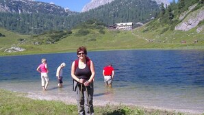 A lake with mountains in the background and a building on the shore. - Ferienwohnung Nr. 5, 48 qm, Nichtraucher, 1 Schlafzimmer, Wohnraum/Kochnische, Balkon, Sat-TV, 4 Sterne, max 3 Personen (Anger)