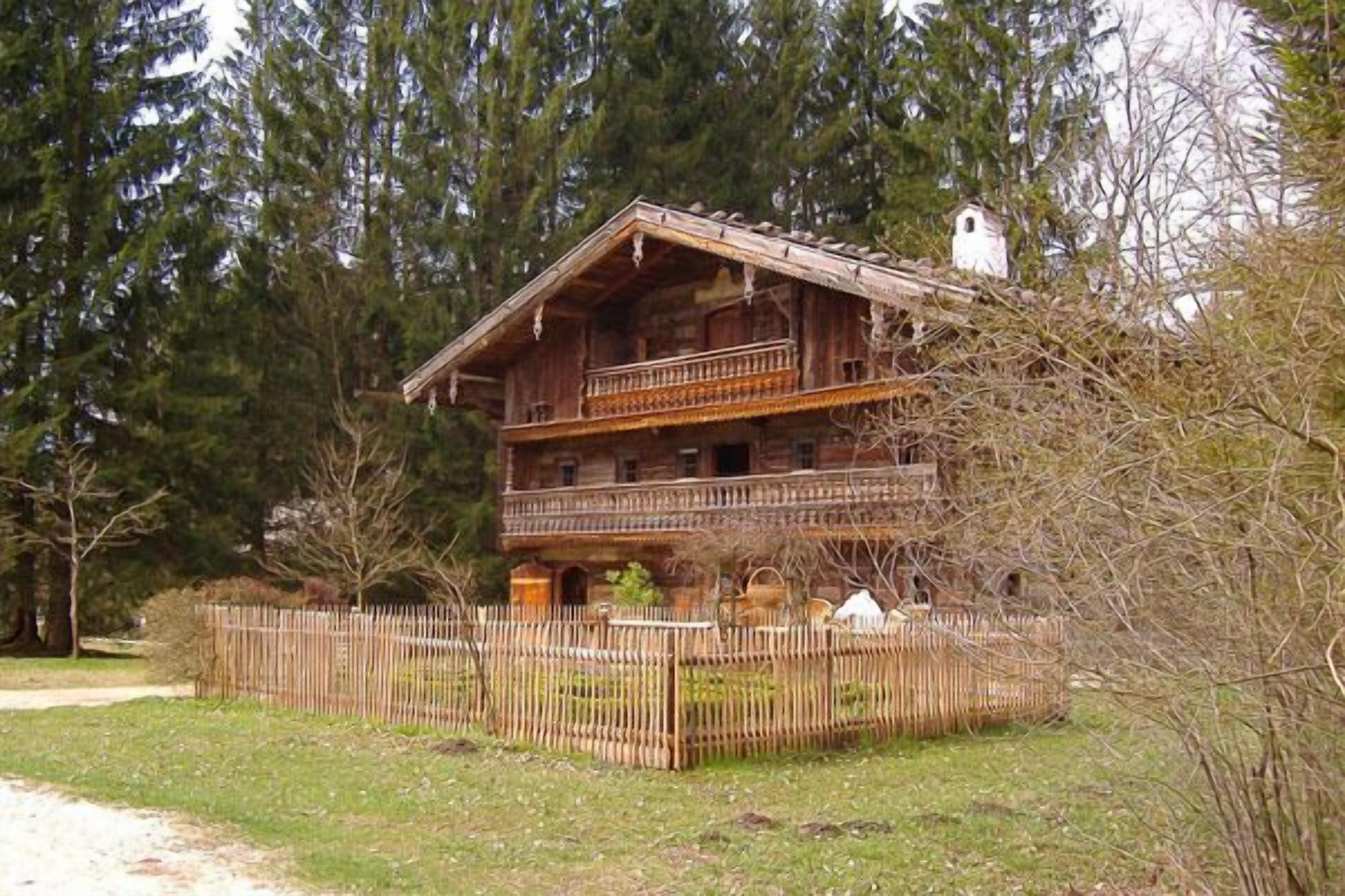 Een houten chalet met twee verdiepingen en een balkon, omgeven door een houten hek en bomen.