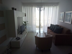 A modern living room with a sofa, a glass coffee table, a TV, and a potted plant.