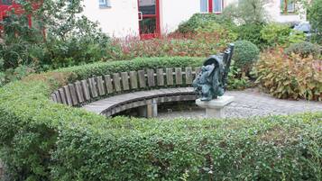 Ein Garten mit einem gewundenen Pfad, einer Statue und einem Gebäude im Hintergrund mit roten Fensterrahmen.