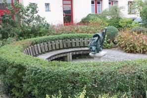 En have med en snoet sti, en statue og en bygning med røde vinduesrammer i baggrunden.
