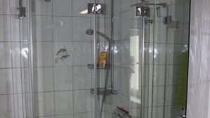 Een badkamer met een douchecabine van glas, een wastafel met spiegel en een groene handdoek.