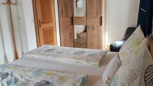 A bedroom with two beds, wooden wardrobe, and a coat rack.