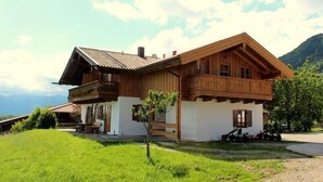 A wooden chalet with a balcony, a small garden, and a mountain backdrop.