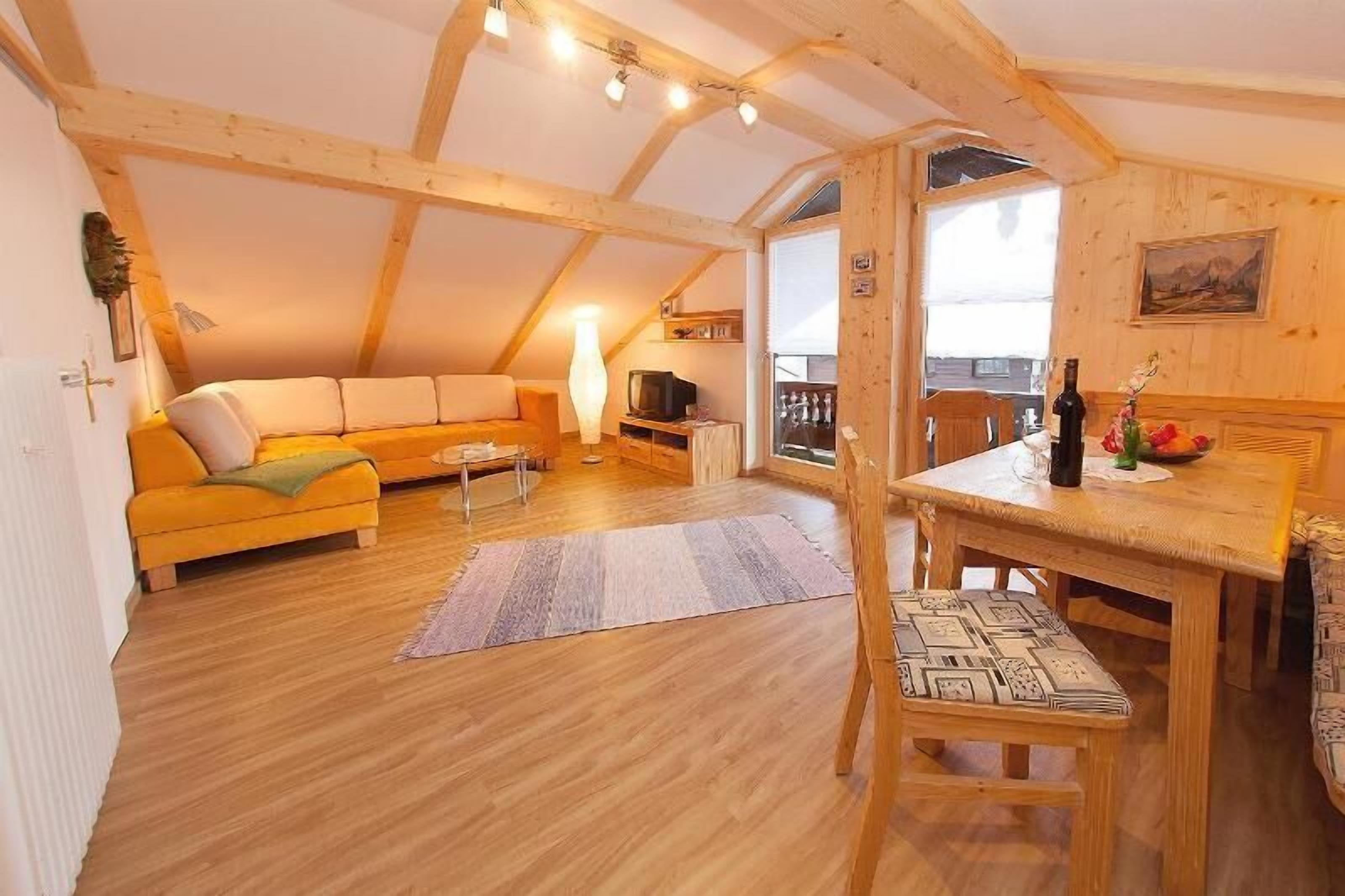 A cozy attic room with a wooden ceiling, a sofa, a dining table, and a television.