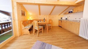 Een gezellig houten huisje met een eethoek, keuken en een groot raam.