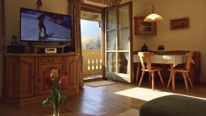 Un salon équipé d’un téléviseur, de meubles en bois, d’un coin repas et d’une porte-fenêtre coulissante donnant sur un espace extérieur.