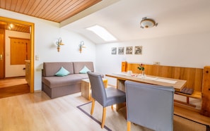 A cozy room with a wooden ceiling, a sofa with cushions, a dining table with chairs, and a small bench.
