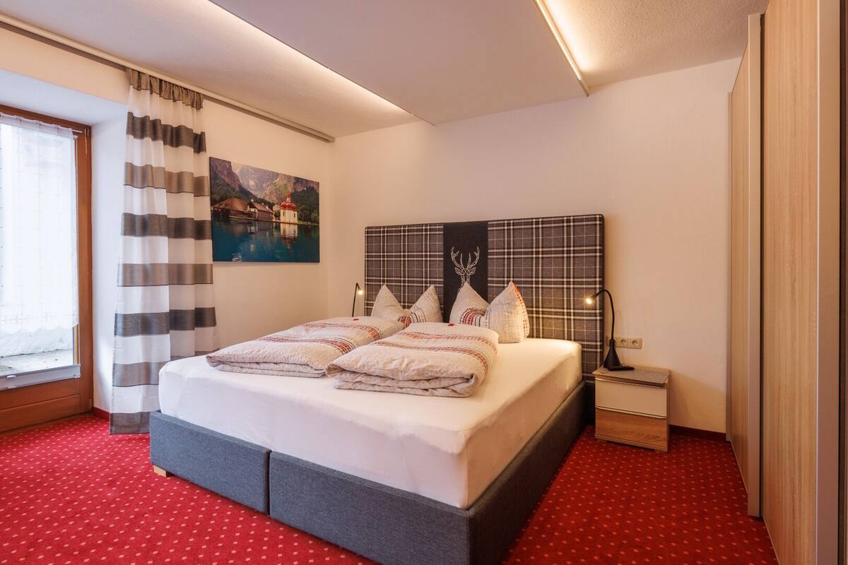 Hotelkamer met een groot bed, nachtkastje, lamp, schilderij aan de muur en een raam met gordijnen.