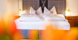A neatly made bed with white linens and decorative pillows, a plaid headboard, and two bedside lamps on wooden nightstands.