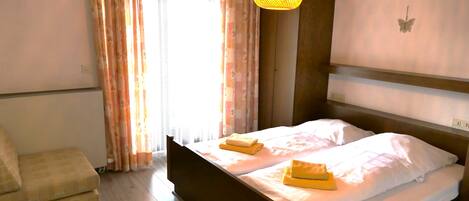 A bedroom with a bed, a chair, a hanging light fixture, and a window with curtains.