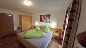 Un dormitorio con cama, armario de madera, mesitas de noche, lámpara de pared y un cuadro.