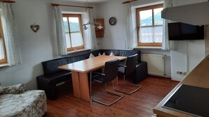 Un comedor con mesa de madera y sillas negras, un sofá negro, y una ventana con cortinas.