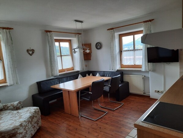 Zona pranzo con tavolo in legno e sedie nere, divano nero e finestra con tende.