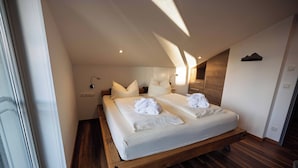 A bedroom with a wooden bed frame, two beds, white linens, a wooden floor, a wall-mounted light, and a window. - Alpenglühn (Berchtesgaden)