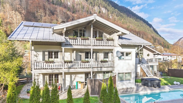 A multi-story building with balconies, a swimming pool, and a mountainous backdrop. - Alpenglühn (Berchtesgaden)