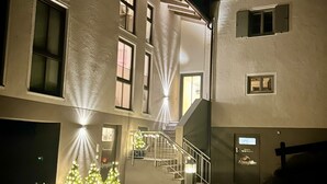A building with multiple windows and a staircase leading to an upper floor. There are potted Christmas trees with lights in the foreground. - Alpenglühn (Berchtesgaden)