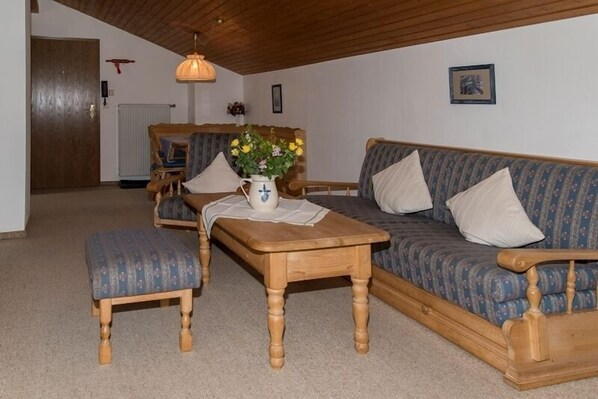 Ein gemütliches Wohnzimmer mit einer Holzsofa, einem passenden Sessel und einem kleinen Holztisch mit einem Blumenstrauß.