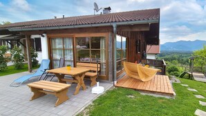 Une maison en bois avec un patio, une table à manger et des bancs.