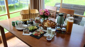 Une table de petit-déjeuner agrémentée d’un panier en osier, d’un arrangement floral et d’une variété d’aliments et de boissons.