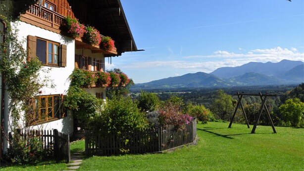 Un chalet à deux étages doté d’un balcon orné de fleurs, d’une clôture en bois et d’une cour verdoyante avec une balançoire.