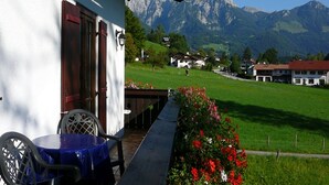 A balcony with a table and chairs, overlooking a green field and mountains.