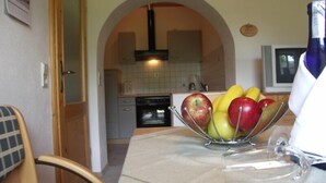 Una cocina con comedor, que incluye una mesa con frutero, una silla y un televisor.