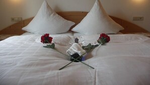 Una cama bien hecha con sábanas blancas, dos almohadas grandes de color blanco y dos rosas rojas sobre la cama.