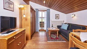 A cozy living room with a wooden ceiling, a TV, a sofa, and a dining table. - (5) Two-room vacation apartment, approx. 42 m², separate kitchen and balcony (Reit im Winkl)