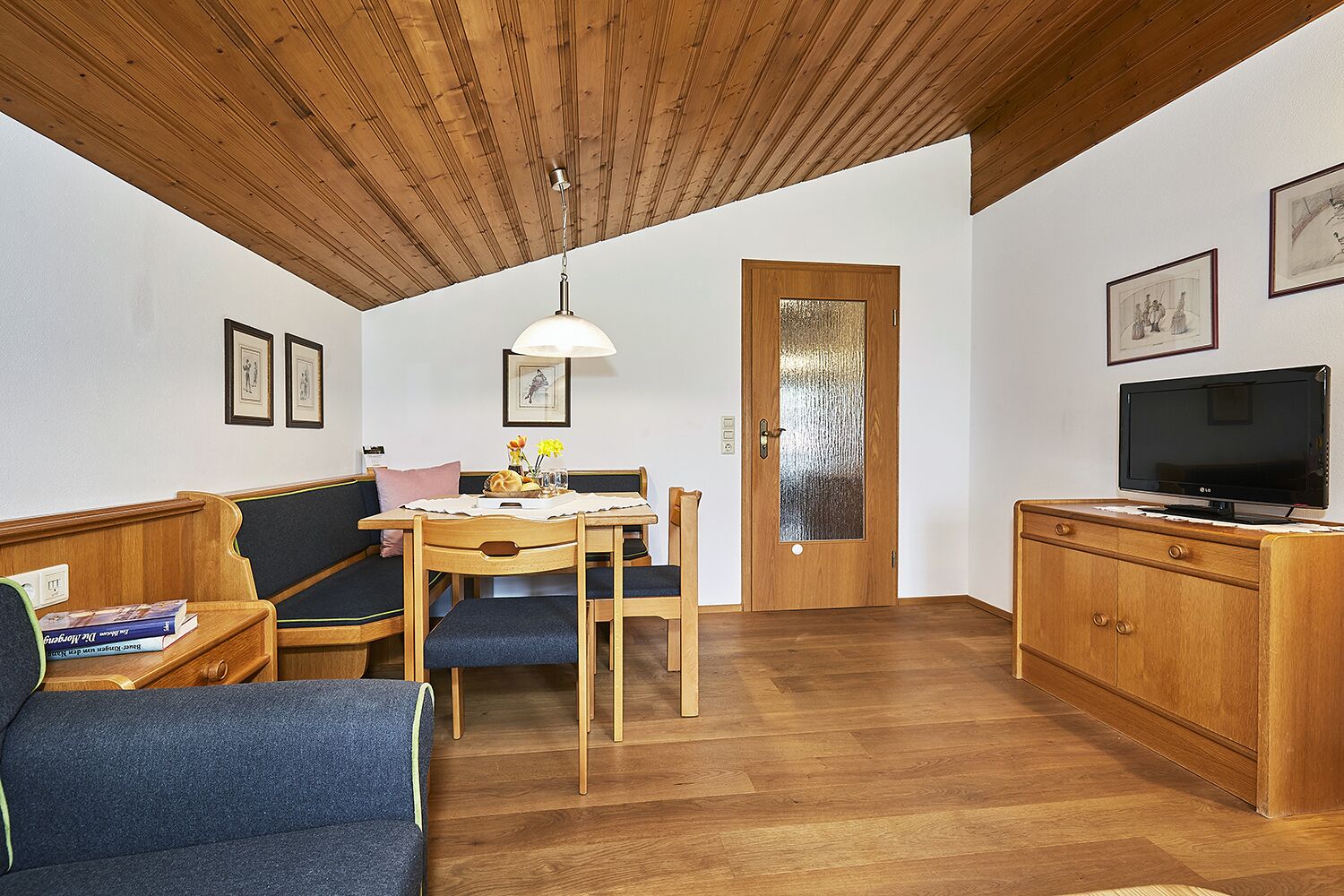 Une pièce chaleureuse avec un plafond en bois, une table à manger avec des chaises, un canapé, un téléviseur et un meuble.