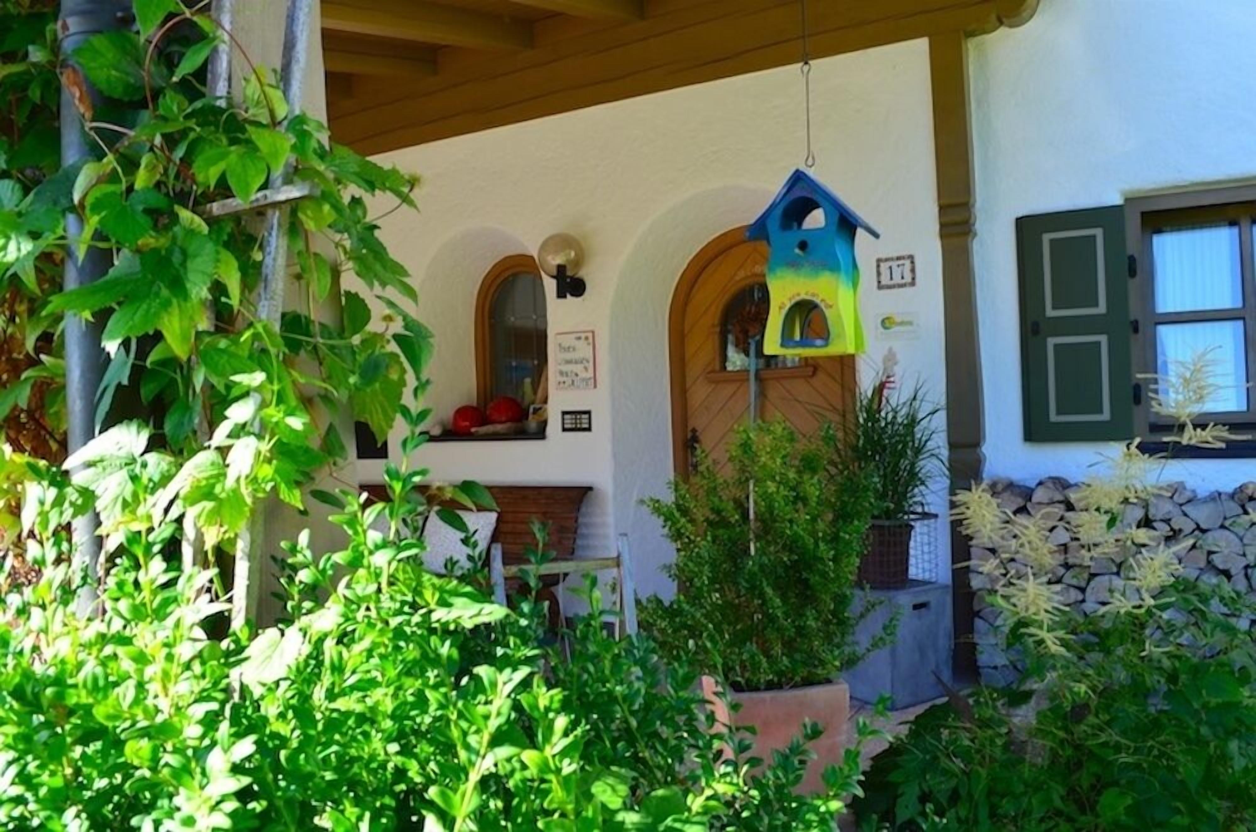 Un porche cubierto con un comedero para pájaros, un muro de piedra y follaje.