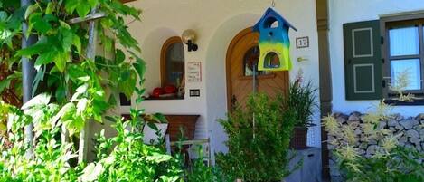 A covered porch with a birdhouse, a stone wall, and greenery.