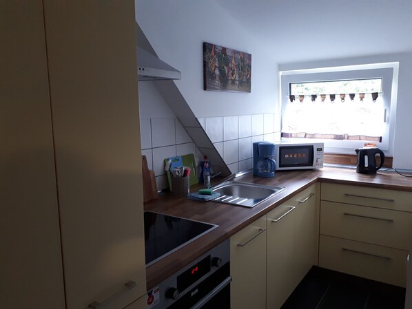 A compact kitchen with a built-in oven, a microwave, a coffee maker, and a kettle on the counter. - Sarahs Klein aber fein (Neunkirchen)