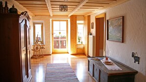 A wooden interior with a wooden ceiling, a door leading outside, a window with a view, and a painting on the wall. - Ferienwohnung Erdgeschoß (Reit im Winkl)