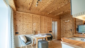 A wooden interior with a dining table, two chairs, a small ottoman, and a kitchen area with a sink and cabinets. - Ferienwohnung Erdgeschoß (Reit im Winkl)