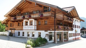 A wooden building with balconies, a sign reading "Beim Ruhhaus," and a mountain view in the background. - Ferienwohnung Erdgeschoß (Reit im Winkl)