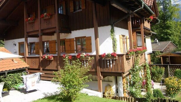 Un chalet traditionnel en bois, doté de plusieurs balcons, d’une façade blanche et de fleurs rouges.