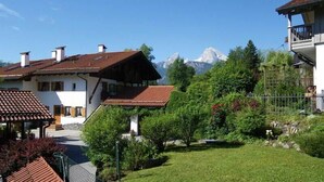 Un chalet traditionnel, doté d’un toit en pente, entouré d’une végétation luxuriante et avec une chaîne de montagnes en toile de fond.