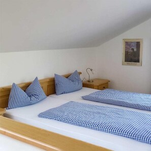 A bedroom with a wooden headboard, a single bed with blue checkered bedding, a nightstand with a lamp, and a framed picture on the wall.