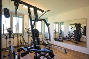 Ein Fitnessraum mit unterschiedlichen Trainingsgeräten, darunter ein Kabelzuggerät und ein Ergometer.
