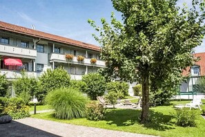 Een hotel met een tuin, een boom en een rode parasol.