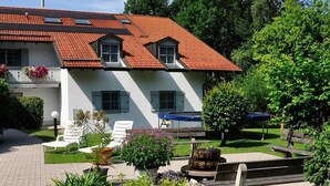A two-story house with a red-tiled roof, white walls, and a garden area with outdoor furniture.