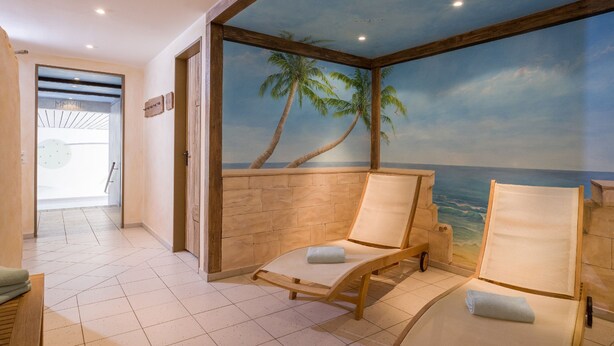 A room with two wooden lounge chairs, a tiled floor, a mural of a beach scene, and a wooden door.