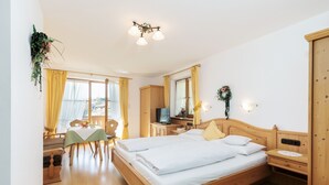 A bedroom with a wooden bed, a desk with a chair, a television, and a window with curtains. - One-room apartment 30sqm, shower/WC, kitchen, balcony (Reit im Winkl)